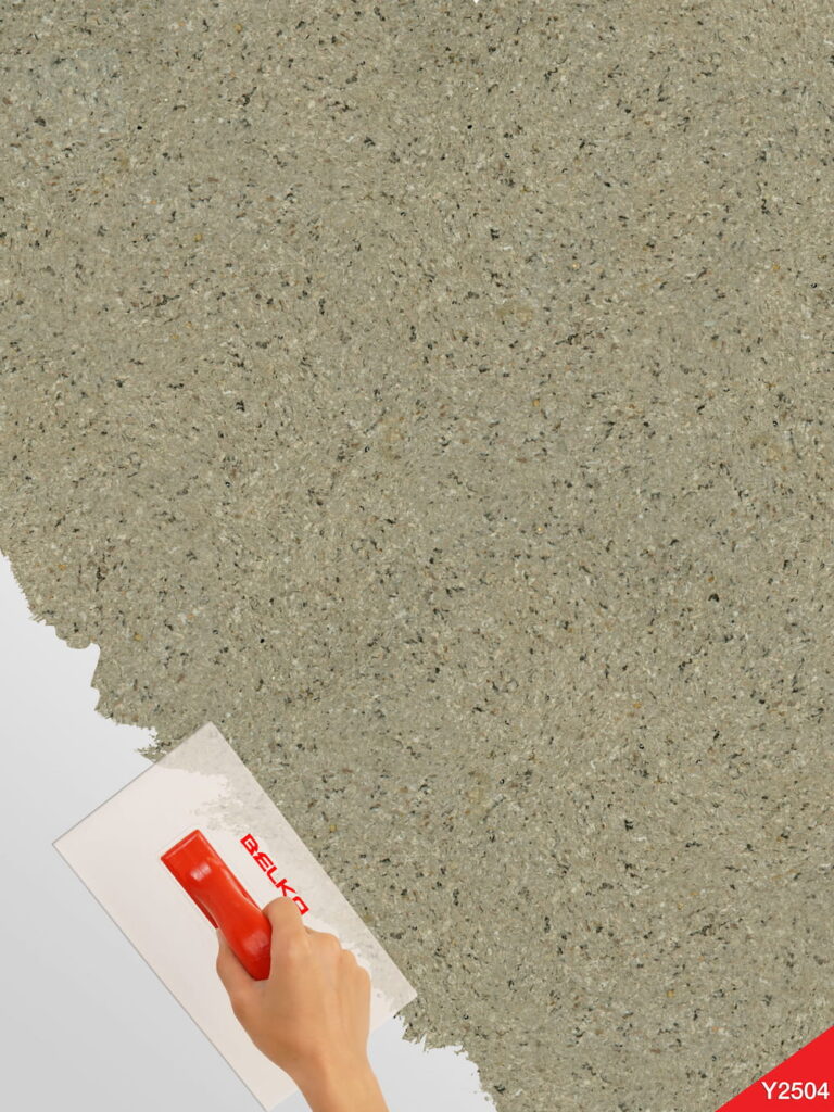 Wüstentaupenfarbene Belka Y2504 Tapete, aufgetragen auf eine moderne Wohnzimmerwand. Die warme, erdige Textur harmoniert mit minimalistischen Möbeln in Grau und Weiß, schafft eine gemütliche, stilvolle Atmosphäre. Im Licht schimmert die Tapete sanft und betont die natürliche Eleganz des Raumes