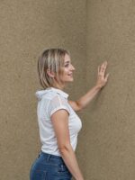 Belka Y2505 Tapete Caramelized auf einer modernen Wohnzimmerwand. Die warme, strukturierte Oberfläche harmoniert mit Holz- und Cremetönen, schafft eine gemütliche, elegante Atmosphäre. Im Licht schimmert die Tapete sanft und betont natürliche Wärme.