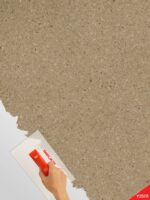 Belka Y2505 Tapete Caramelized auf einer modernen Wohnzimmerwand. Die warme, strukturierte Oberfläche harmoniert mit Holz- und Cremetönen, schafft eine gemütliche, elegante Atmosphäre. Im Licht schimmert die Tapete sanft und betont natürliche Wärme.