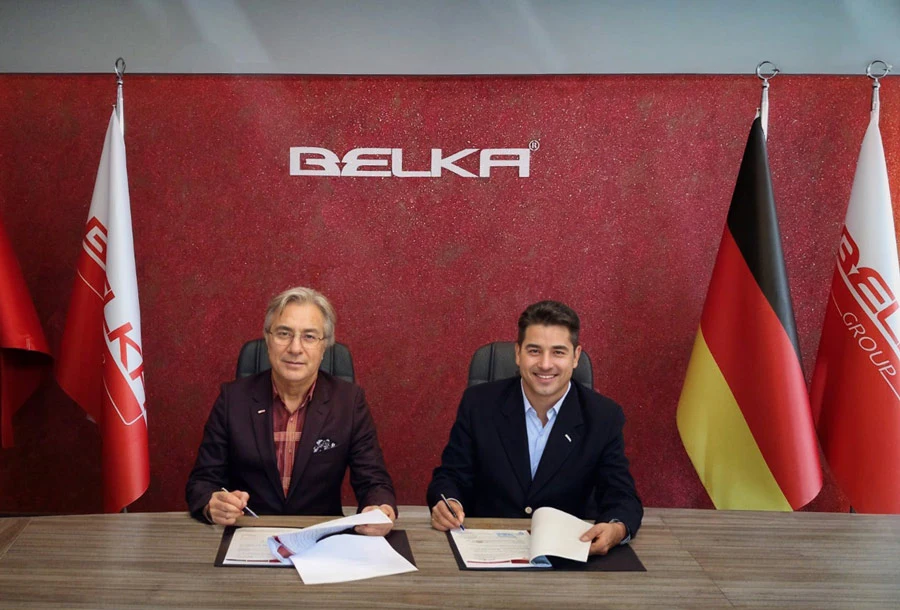 Two men signing a partnership agreement to become Belka Distributorship or representatives, with Belka branding and flags in the background.